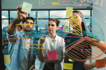 Skilled project manager pointing at glass wall while coworker thinking about plan. Diverse business team working together, brainstorming marketing idea or business plan. Creative start up. Tracery.