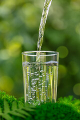 water pouring into glass on moss with green natural background