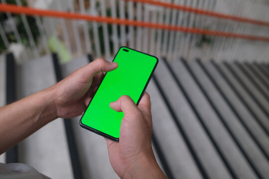 smartphone with green screen in hands of person against background of stairs