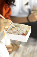 Crop shot from above of man and woman taking sushi with chopsticks from carton box