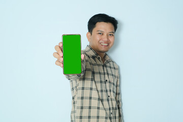 Young Asian man showing green screen his mobile phone with selective focus. Wearing a cream flannel shirt