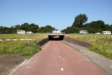 Dutch highway N9 near Alkmaar with bridge over cycle path. Traffic, cars, camper, caravan. Blue sky. Summer, July, Netherlands