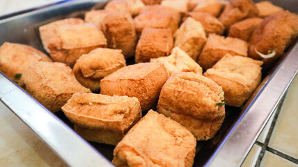 A close up of a tray filled with fried tofu cubes. The tofu is golden brown and crispy, ready to be enjoyed as a delicious snack or part of a meal. Close up of Golden Fried Tofu Background.