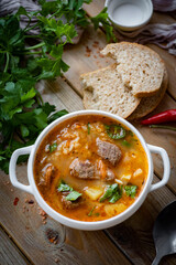 A hearty lunch for the whole family: spicy soup with beef, vegetables and fresh herbs in a white plate on a wooden background. Close-up. Vertical photo