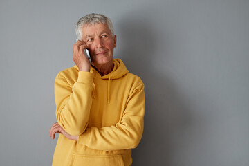 Handsome mature gray haired man wearing yellow hoodie answering phone call standing isolated over...