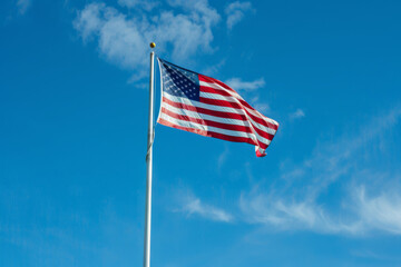 Obraz premium A vibrant American flag waves proudly against a backdrop of a bright blue sky with wispy white clouds