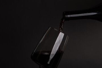glass with red or white wine and grape isolated on black backdrop.pouring alcohol from bottle,...