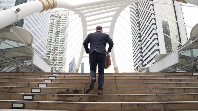 Smart caucasian businessman walking up stairs surrounded by urban view. Back view of ambitious project manager finding challenging job or investment opportunity at city with modern building. Urbane.