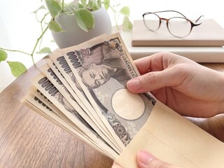 机上で封筒に入った10万円を持つ女性の手元