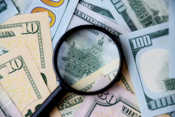 Big amount of US dollar bills in different nominations and magnifying glass. Many dollar banknotes under natural light