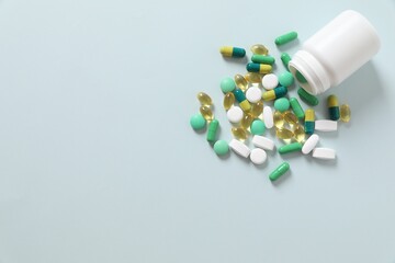 Various medicines and health pills poured from a medical white bottle, healthcare and medical top view on a colorful blue background.