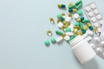 Various medicines and health pills poured from a medical white bottle, healthcare and medical top view on a colorful blue background.