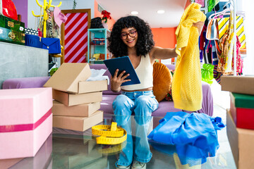 Beautiful young hispanic woman managing her home clothing e-commerce business from home - Female...