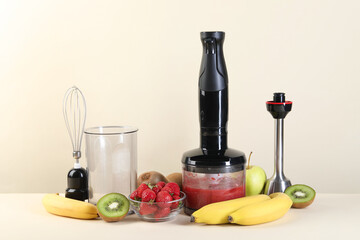 Hand blender kit, mixture of ingredients and fresh fruits on beige background