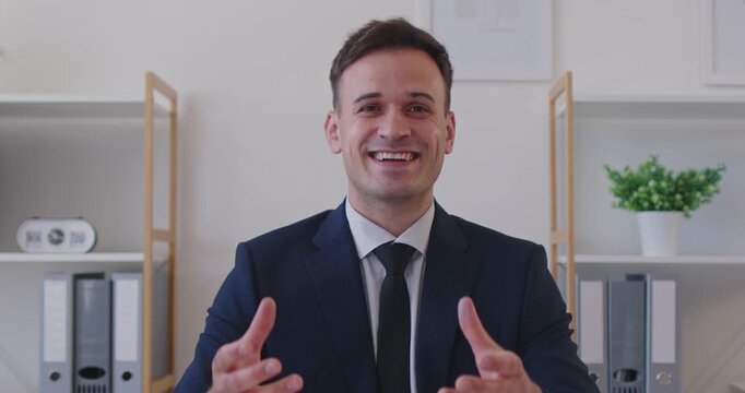 Video portrait of businessman sharing his expertise during webinar. Happy smiling man in suit sitting in office, looking at camera and speaking. Video conference, online business communication concept