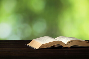 Bible on wooden table against blurred green background, space for text. Religion of Christianity