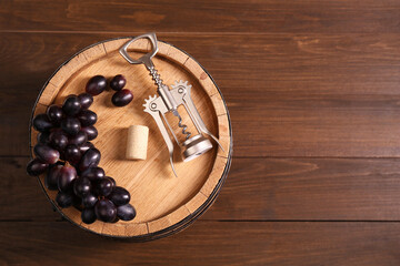 Wing corkscrew, cork, grapes and barrel on wooden table, top view. Space for text