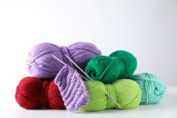 Many soft skeins of yarn, knitted fabric and needles on light grey background