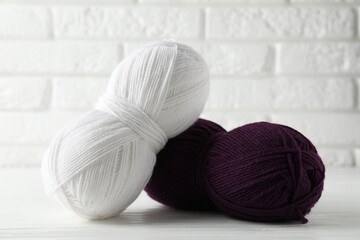 Skeins of colorful yarns on white wooden table against brick wall, closeup