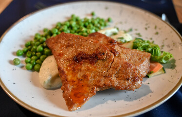 Roasted meat and vegetables served on a plate in a restaurant. Beef and peas.