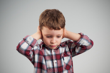 The boy covers his ears with his hands, expressing his reluctance to hear noise, conveying feelings...