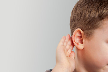 Fototapeta premium The boy, with his hand to his ear, listens attentively, conveying emotional sincerity and childish curiosity