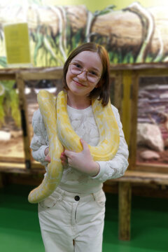 A child holds a large yellow python around their neck at a reptile exhibit, showcasing the interactive and educational nature of the display.
