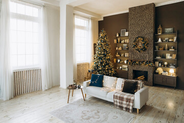 Cozy living room decorated for Christmas with a white sofa, a beautifully adorned Christmas tree, a fireplace with festive wreath, bookshelves, and large windows with sheer curtains