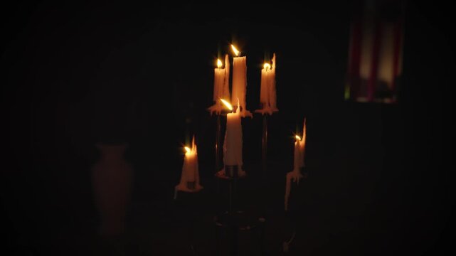 close-up detail shot, medieval antique old style candlestick with burning candles stands in dark room black background. Yellow orange wax candle warm magic light fantasy gothic mystical atmosphere 4k