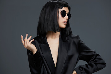 Asian woman in black suit and sunglasses posing confidently on a gray background, exuding sophistication and modern style
