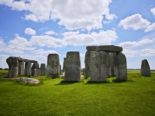 Naklejka premium Stonehenge ruins with large ancient stones against a blue sky in Wiltshire, England, showcasing a prehistoric landmark surrounded by grass and landscape