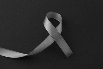 Grey awareness ribbon on black background, top view