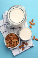 Glass of almond milk, jug and almonds on light blue wooden table, top view