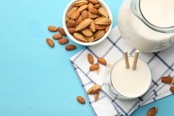 Glass of almond milk, jug and almonds on light blue wooden table, top view. Space for text
