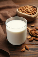 Glass of almond milk and almonds on wooden table
