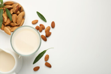Fresh almond milk in glass, nuts, green leaves and pitcher on white background, flat lay. Space for text
