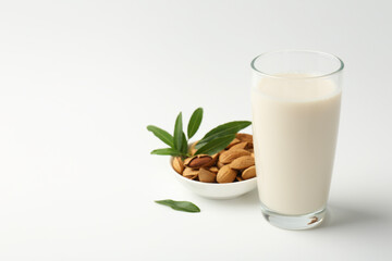 Fresh almond milk in glass, nuts and green leaves on white background, space for text