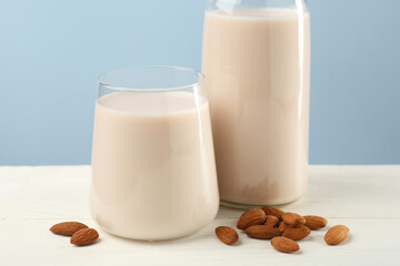 Fresh almond milk in glass, bottle and nuts on white wooden table