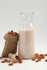 Fresh almond milk in carafe, nuts, scoop and burlap sack on white background