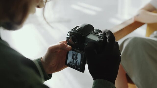 Hands of male photographer wearing glove taking black-and-white portraits of female model with medium format film camera during studio photo shoot. Close-up view