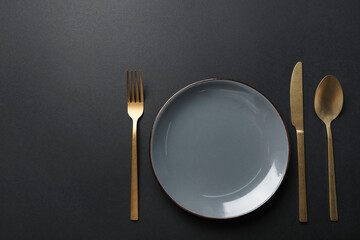 Elegant golden cutlery and plate on black background, flat lay. Space for text