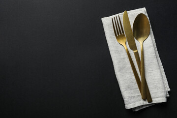 Elegant golden cutlery and napkin on black background, top view. Space for text