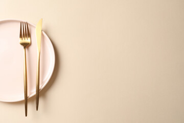 Stylish golden cutlery and plate on beige background, top view. Space for text