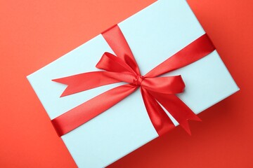 Gift box with red bow on coral background, top view