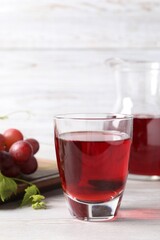 Tasty grape juice in glass, leaves and berries on light wooden table