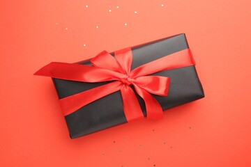Gift box with red bow and confetti on coral background, top view