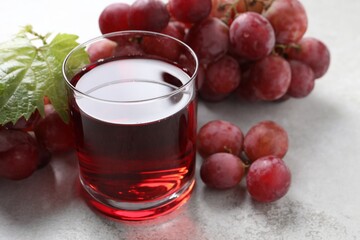 Tasty grape juice in glass, leaf and berries on light textured table, closeup