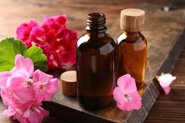 Geranium essential oil in bottles and beautiful flowers on wooden table