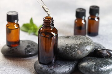 Essential oil dripping from pipette into bottle on table, closeup