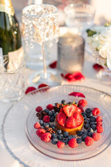 Close up selective focus desserts with sweet fresh strawberries, raspberries and blueberries and empty glasses. Summer romantic evening under the open sky.